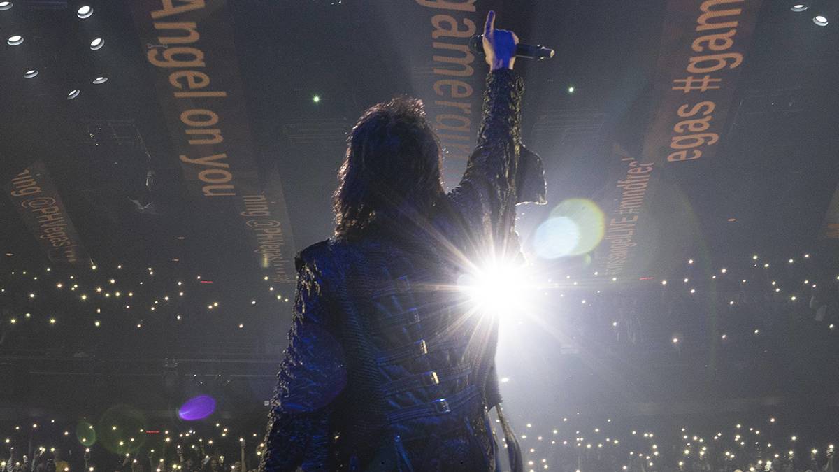 Man standing with his arm raised on a stage looking out at a crowd